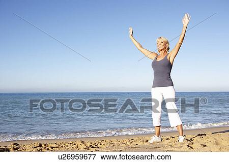 Stock Photo - Senior Woman In Fitness Clothing Stretching On Beach. Fotosearch