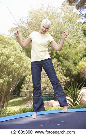 Stock Image - Senior Woman Jumping On Trampoline In Garden. Fotosearch