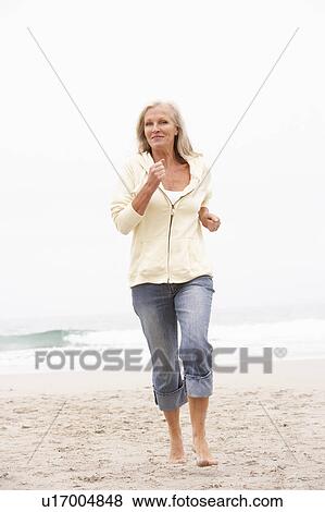 Stock Photo - Senior Woman On Holiday Running Along Winter Beach. Fotosearch