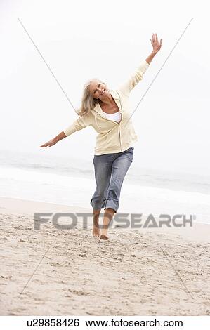 Stock Photograph - Senior Woman On Holiday Running Along Winter Beach. Fotosearch