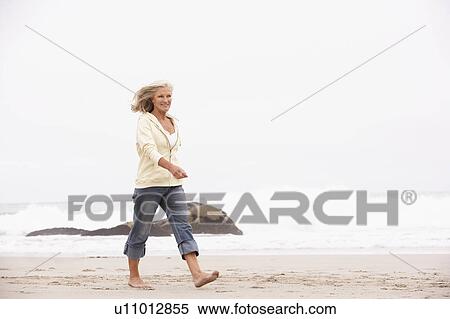 Stock Photography - Senior Woman On Holiday Running Along Winter Beach. Fotosearch