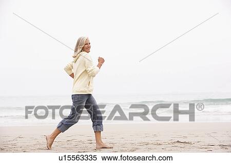 Stock Photography - Senior Woman On Holiday Running Along Winter Beach. Fotosearch