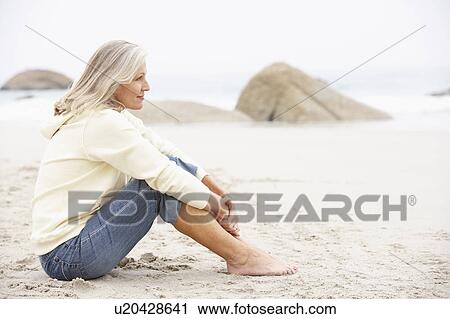 Stock Image - Senior Woman On Holiday Sitting On Winter Beach. Fotosearch