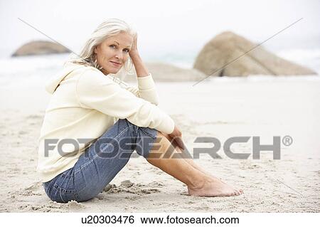 Stock Photograph - Senior Woman On Holiday Sitting On Winter Beach. Fotosearch