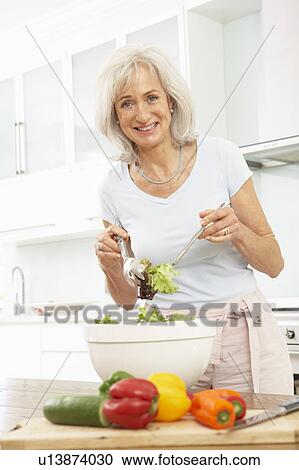 Stock Image - Senior Woman Preparing Salad In Modern Kitchen. Fotosearch