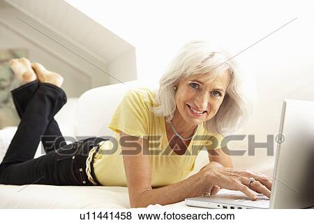 Senior Woman Using Laptop Relaxing Sitting On Sofa At Home View Large Photo Image Stock Photo - Senior Woman Using Laptop Relaxing Sitting On Sofa At Home. Fotosearch