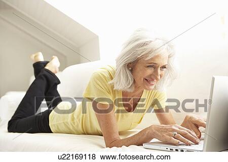 Stock Photo - Senior Woman Using Laptop Relaxing Sitting On Sofa At Home. Fotosearch