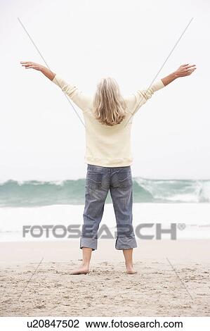 Stock Image - Senior Woman With Arms Outstretched On Winter Beach. Fotosearch