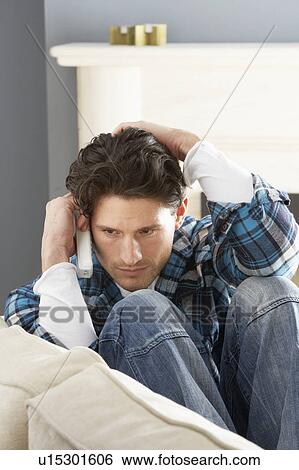 Stock Photograph - Stressed Man Sitting On Sofa At Home Talking On Phone. Fotosearch
