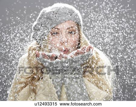 Stock Photography - Teenage Girl Wearing Warm Winter Clothes And Hat Blowing Snow In Studio. Fotosearch
