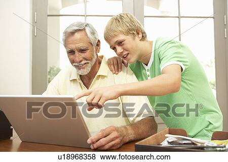Stock Photo - Teenage Grandson Helping Grandfather To Use Laptop At Home. Fotosearch