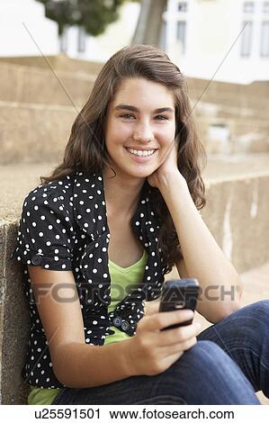 Stock Image - Teenage Student Sitting Outside On College Steps Using Mobile Phone. Fotosearch