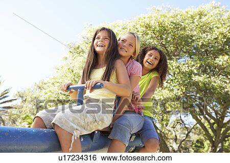 Stock Photograph - Three Girls Riding On See Saw In Playground. Fotosearch