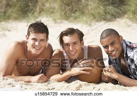 Three Young Men Relaxing On Beach With Football Together View Large Photo Image Stock Photo - Three Young Men Relaxing On Beach With Football Together. Fotosearch