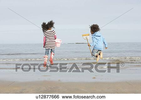 Stock Photograph - Two Children Playing By Sea On Winter Beach. Fotosearch