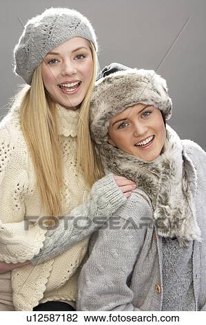 Stock Image - Two Fashionable Teenage Girls Wearing Cap And Knitwear In Studio In Front Of Christmas Tree. Fotosearch