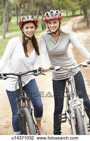 Two Female friends riding bikes in park View Large Photo Image Stock Image - Two Female friends riding bikes in park. Fotosearch