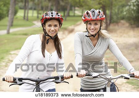 Two Female friends riding bikes in park View Large Photo Image Stock Image - Two Female friends riding bikes in park. Fotosearch