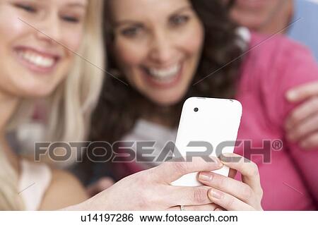 Stock Photograph - Two Girlfriends Looking At Pictures On Smartphone At Home. Fotosearch