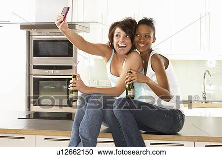 Stock Image - Two Girlfriends Taking Photo With Digital Camera In Modern Kitchen. Fotosearch