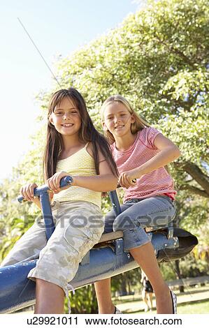 Stock Image - Two Girls Riding On See Saw In Playground. Fotosearch