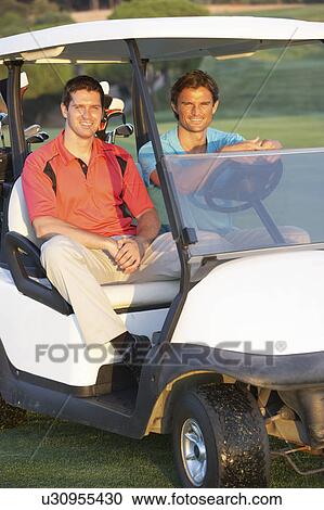 Stock Image - Two Male Golfers Riding In Golf Buggy On Golf Course. Fotosearch