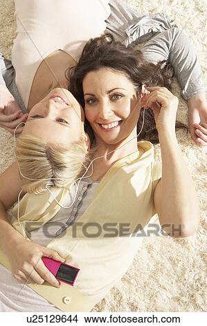 Two Women Listening To MP3 Player On Headphones Together Relaxing Laying On Rug At Home View Large Photo Image Picture - Two Women Listening To MP3 Player On Headphones Together Relaxing Laying On Rug At Home . Fotosearch
