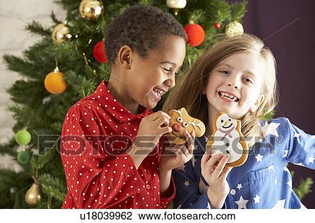 Two Young Children Eating Christmas Treats In Front Of Christmas Tree View Large Photo Image Stock Image - Two Young Children Eating Christmas Treats In Front Of Christmas Tree. Fotosearch