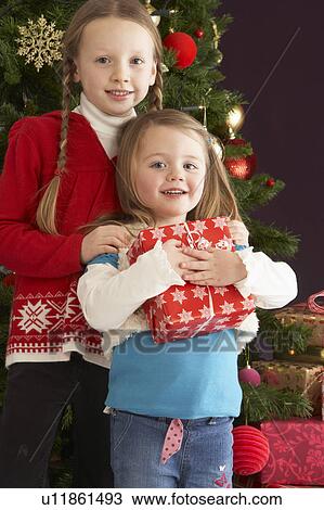 Stock Image - Two Young Girls With Presents In Front Of Christmas Tree. Fotosearch
