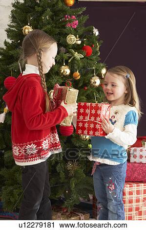 Stock Image - Two Young Girls With Presents In Front Of Christmas Tree. Fotosearch