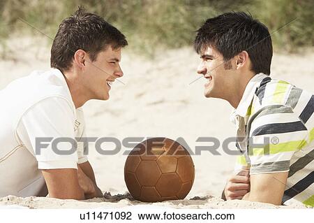 Two Young Men Relaxing On Beach With Football Together View Large Photo Image Stock Image - Two Young Men Relaxing On Beach With Football Together. Fotosearch
