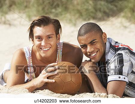 Two Young Men Relaxing On Beach With Football Together View Large Photo Image Stock Image - Two Young Men Relaxing On Beach With Football Together. Fotosearch