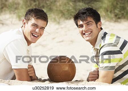 Stock Photo - Two Young Men Relaxing On Beach With Football Together. Fotosearch