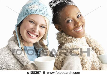Stock Photograph - Two Young Women Wearing Warm Winter Clothes Holding Snowball In Studio. Fotosearch