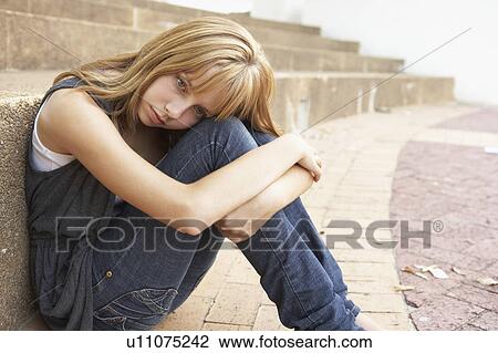 Stock Image - Unhappy Female Teenage Student Sitting Outside On College Steps Using Mobile Phone. Fotosearch