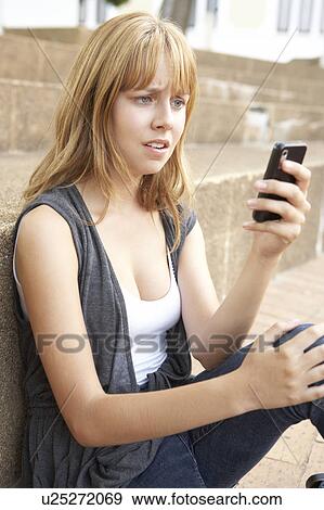 Stock Photo - Unhappy Female Teenage Student Sitting Outside On College Steps Using Mobile Phone. Fotosearch