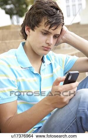 Unhappy Male Teenage Student Sitting Outside On College Steps Using Mobile Phone View Large Photo Image Picture - Unhappy Male Teenage Student Sitting Outside On College Steps Using Mobile Phone. Fotosearch