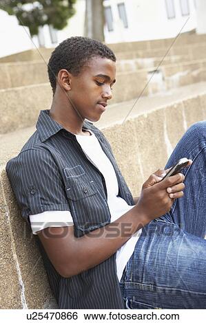 Stock Photograph - Unhappy Male Teenage Student Sitting Outside On College Steps Using Mobile Phone. Fotosearch