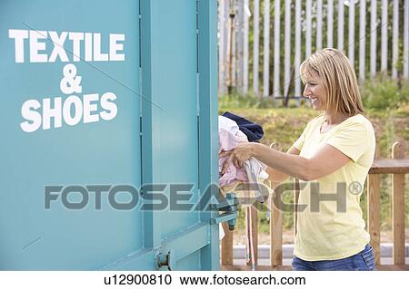 Stock Image - Woman At Recycling Centre Disposing Of Clothing. Fotosearch