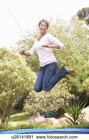 Stock Image - Woman Jumping On Trampoline In Garden. Fotosearch