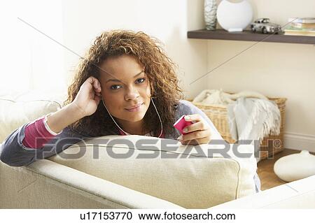Stock Image - Woman Listening To MP3 Player On Headphones Relaxing Sitting On Rug At Home . Fotosearch