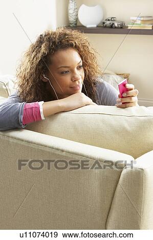 Stock Photo - Woman Listening To MP3 Player On Headphones Relaxing Sitting On Rug At Home . Fotosearch