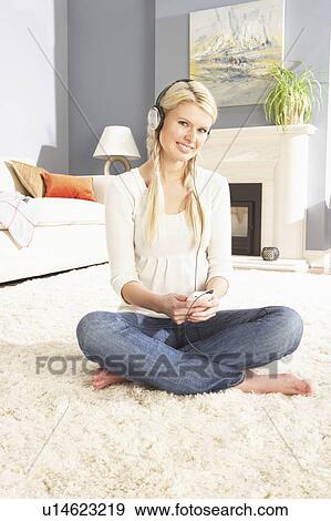 Stock Photo - Woman Listening To MP3 Player On Headphones Relaxing Sitting On Rug At Home . Fotosearch