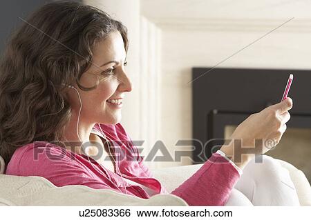 Stock Photograph - Woman Listening To MP3 Player On Headphones Relaxing Sitting On Rug At Home . Fotosearch