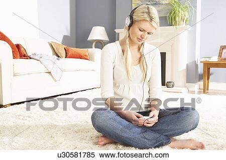 Stock Photography - Woman Listening To MP3 Player On Headphones Relaxing Sitting On Rug At Home . Fotosearch