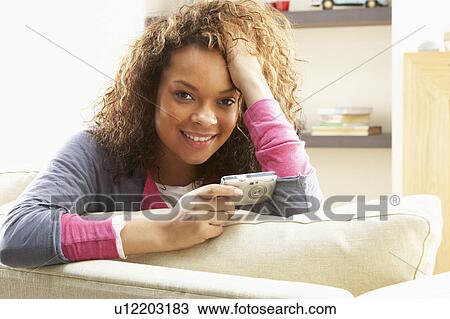 Stock Image - Woman Looking At Pictures On Digital Camera Relaxing Sitting On Sofa At Home . Fotosearch