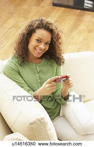 Stock Image - Woman Looking At Pictures On Digital Camera Relaxing Sitting On Sofa At Home. Fotosearch