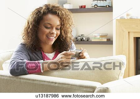 Stock Photograph - Woman Looking At Pictures On Digital Camera Relaxing Sitting On Sofa At Home. Fotosearch