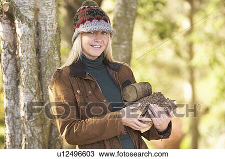 Stock Image - Woman Outdoors In Autumn Woodland Gathering Logs. Fotosearch