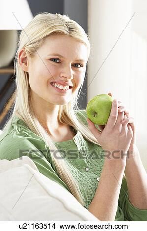 Picture - Woman Relaxing On Sofa Eating Apple At Home. Fotosearch